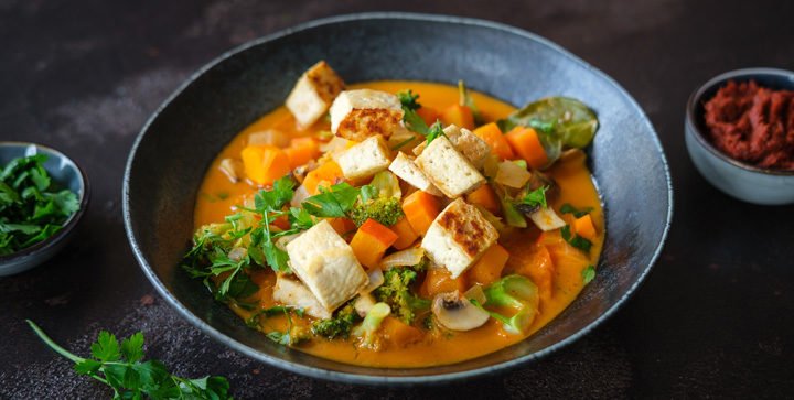 Ein Teller veganes rotes Thai-Curry mit Kürbis, Tofu und buntem Gemüse