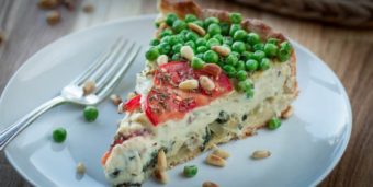 Ein Stück vegane Quiche mit Champignons, Spinat, Erbsen und Tomaten