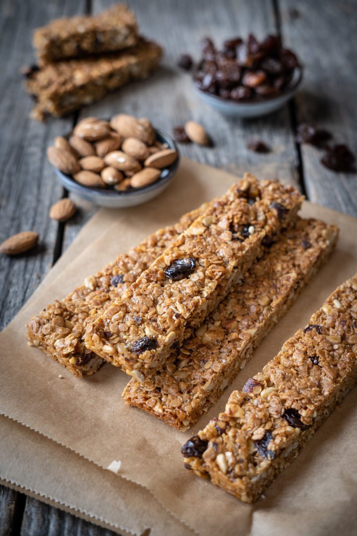 Vier vegane Haferflocken-Nuss-Flapjacks naben einem Schälchen mit Mandeln und Rosinen