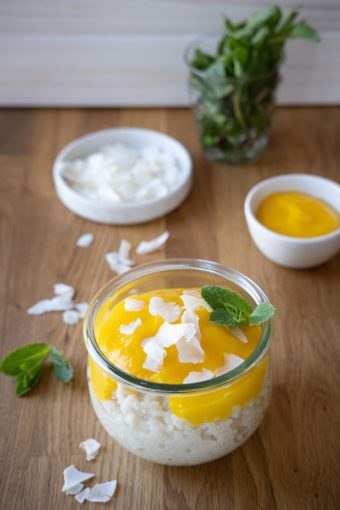 Ein Glas veganer Kokos-Milchreis mit Mangomus und Kokosflocken