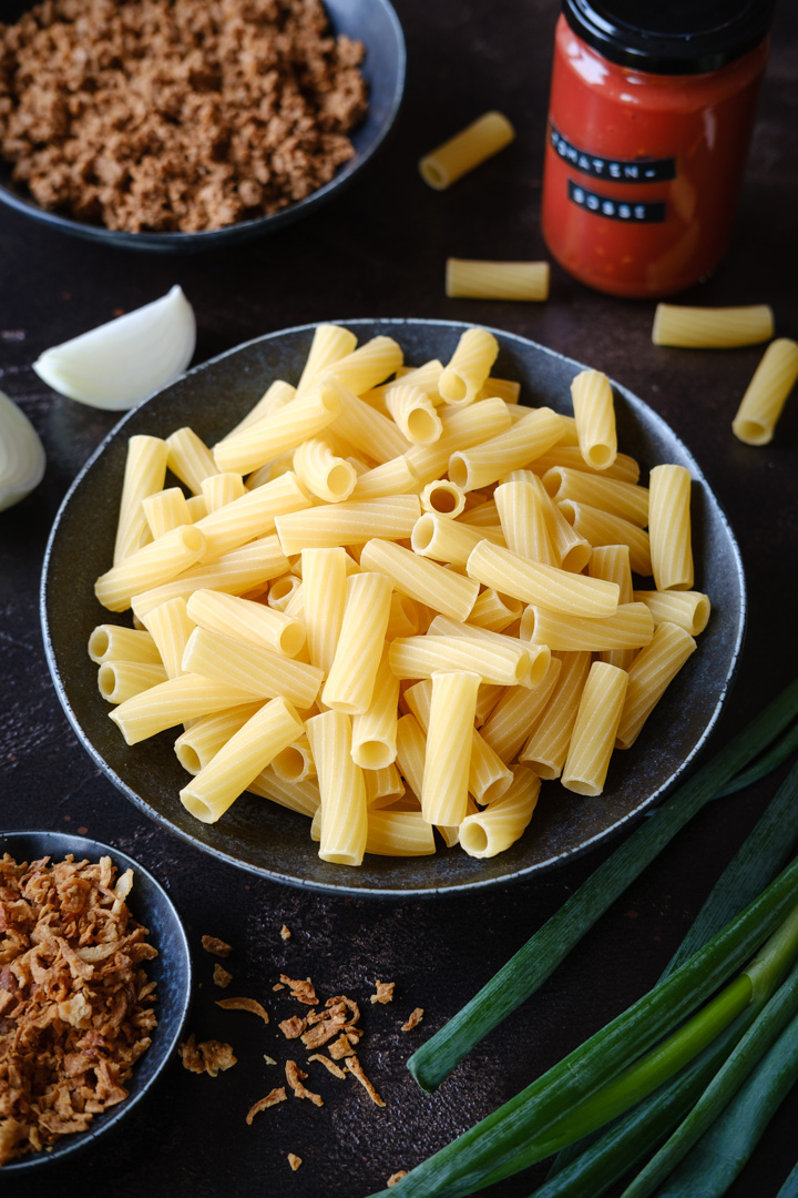 Zutaten für eine vegane Cheeseburger-Pasta: Nudeln, veganes Hackfleisch, Tomatensoße und Röstzwiebeln