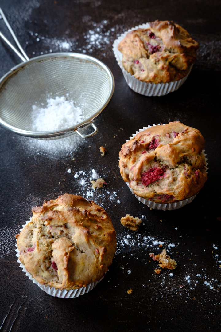 Drei vegane Himbeer-Vanille-Proteinmuffins auf einer dunklen Tischplatte