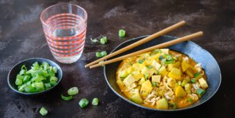 Ein Teller vegane Kokos-Curry-Suppe, ein Schälchen mit Frühlingszwiebeln und ein Glas Wasser