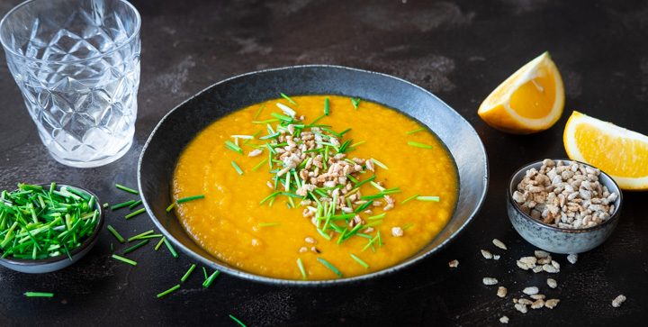 Ein Teller vegane Karotten-Orangen-Suppe mit Schnittlauch und karamellisierten Sonnenblumenkernen