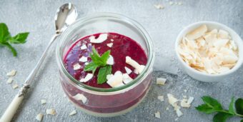 Ein Glasgefäß mit Proteinpudding und einer Soße aus pürierten Beeren steht auf einer weißen Tischplatte.
