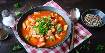 Ein Teller vegane Gulaschsuppe steht auf einer dunklen Tischplatte
