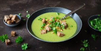 Ein Teller vegane Erbsensuppe mit gerösteten Brotwürfeln steht auf einer dunklen Tischplatte