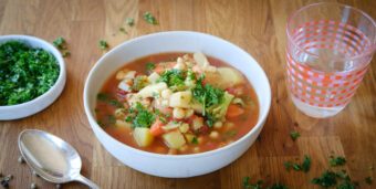 Eine Schale mit einer bunten Gemüsesuppe steht auf einer hölzernen Tischplatte