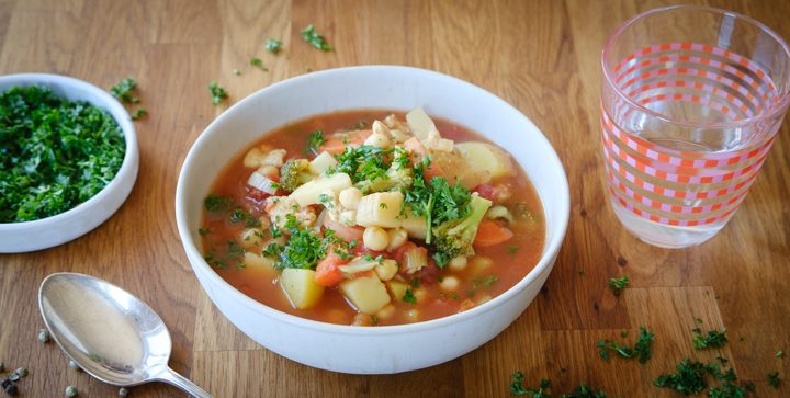 Eine Schale mit einer bunten Gemüsesuppe steht auf einer hölzernen Tischplatte
