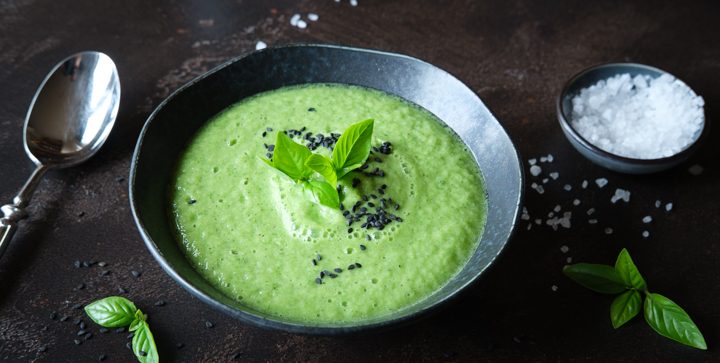 Ein Teller leuchtendgrüner Gurken-Zucchini-Gazpacho steht auf einer dunklen Tischplatte