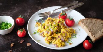 Veganes Rührei aus Mung Dal mit roten Zwiebeln und Schnittlauch auf einem weißen Teller, dazu Tomaten und Brot.